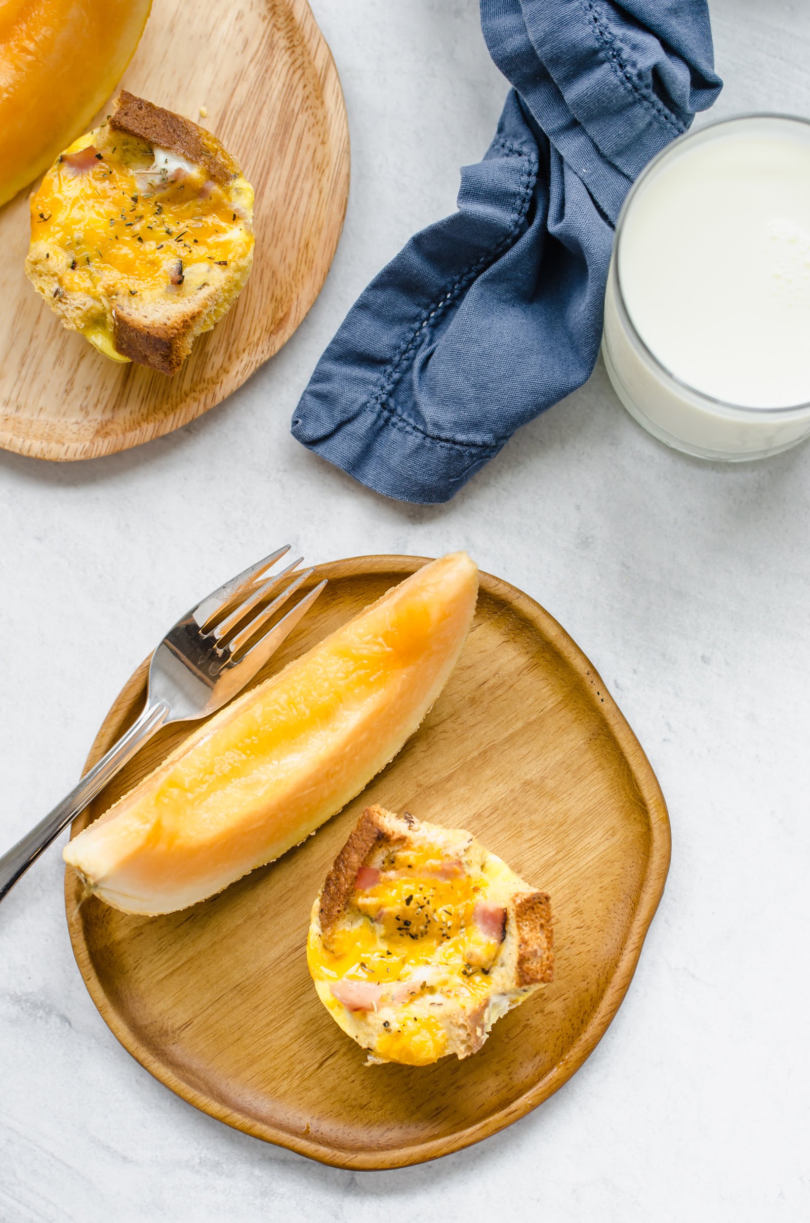 Breakfast casserole muffin on a wooden plate with a slice of cantaloupe and a fork.