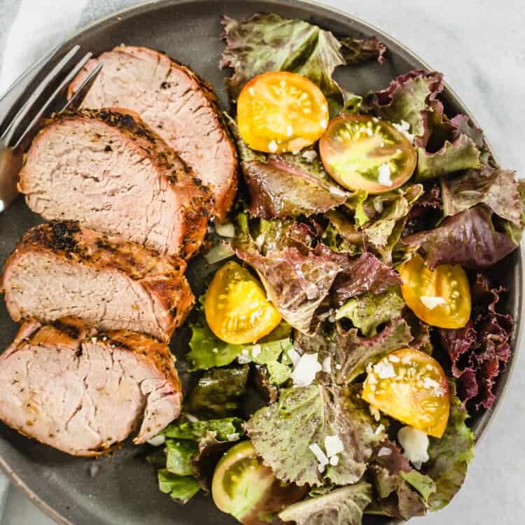 Pork tenderloin sliced and on a plate with salad.