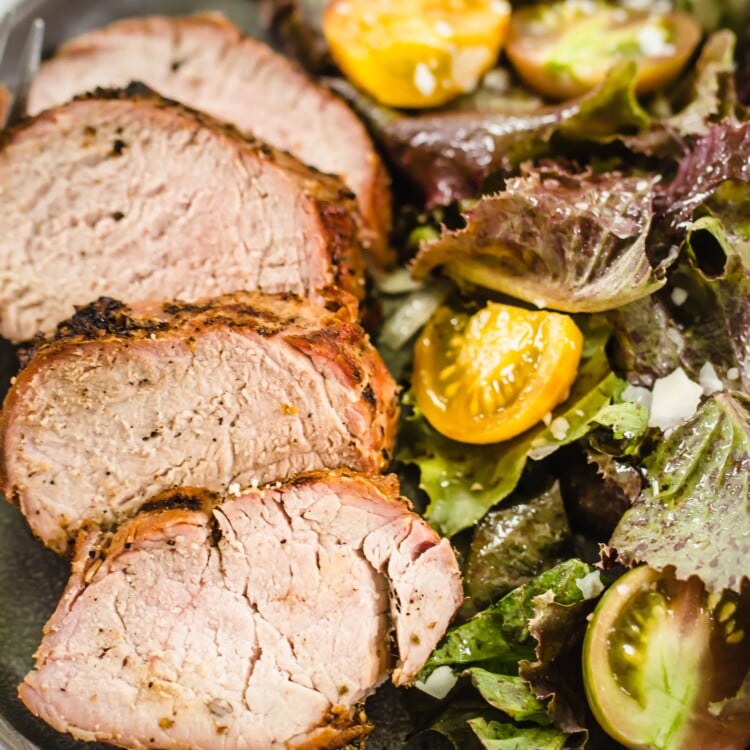 Pork tenderloin sliced and on a plate with salad.