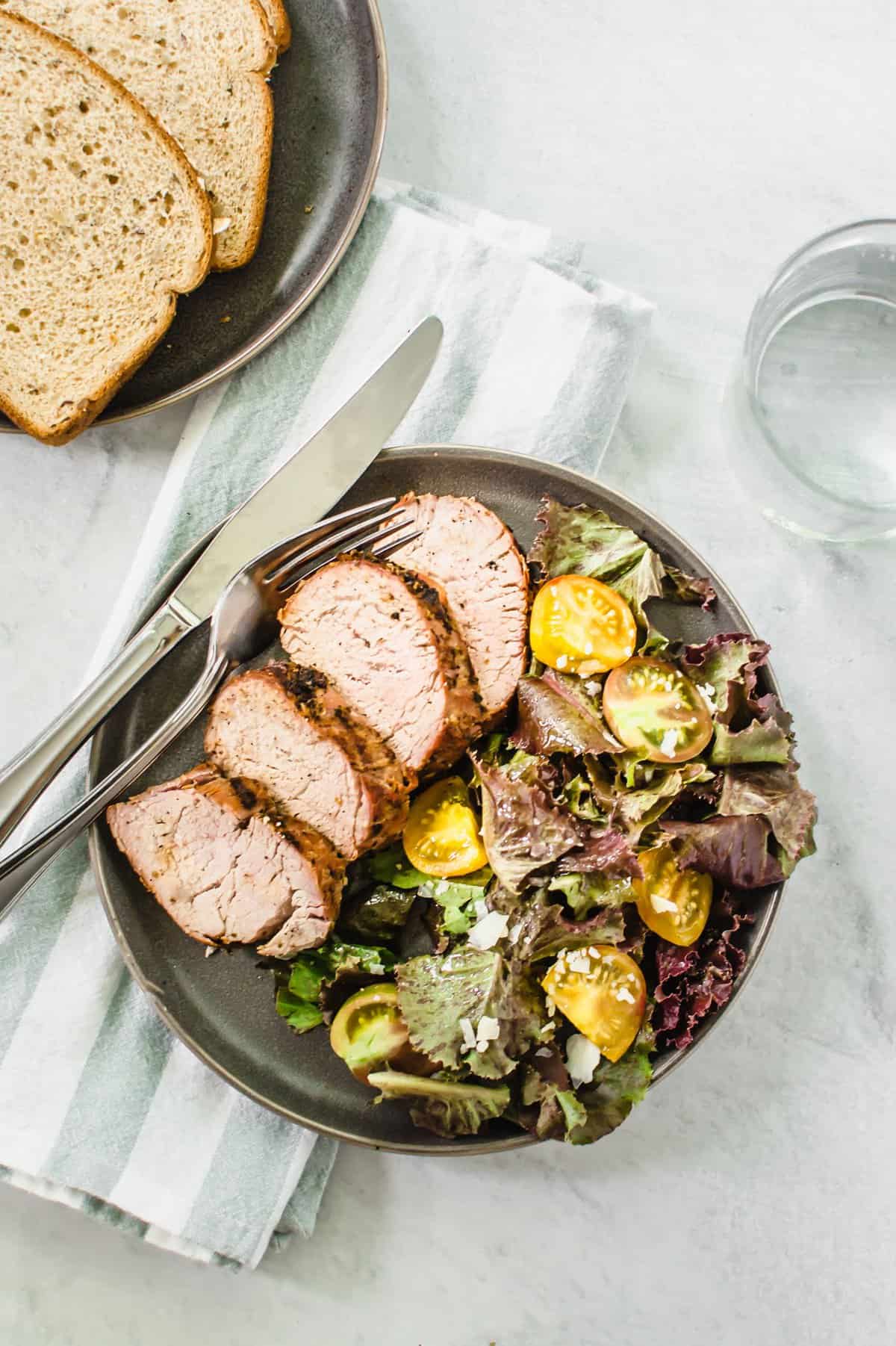 Oven roasted pork tenderloin with seasoning dry rub on a plate with salad.