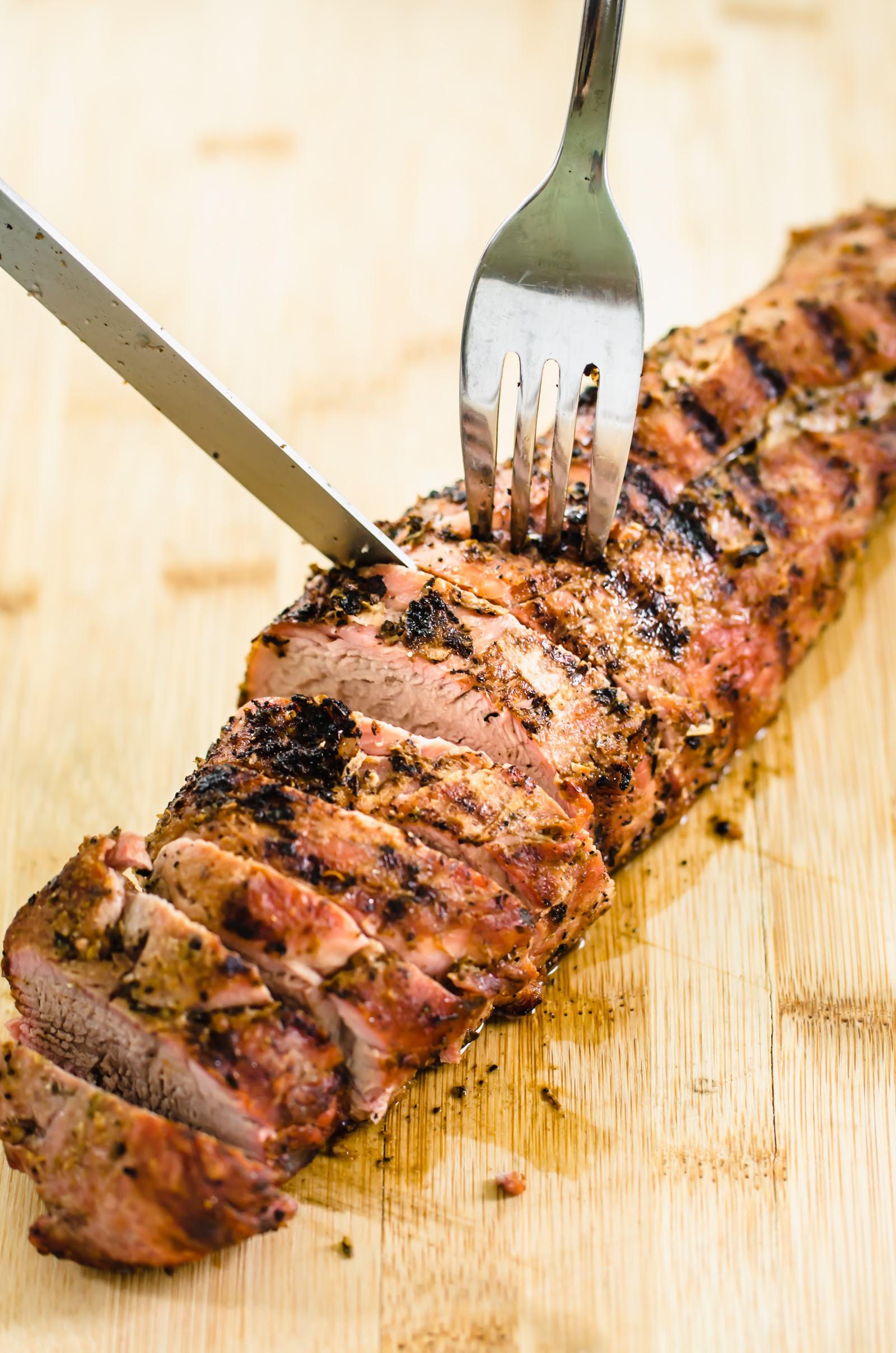 roasted pork tenderloin with seasoning rub being sliced on a wooden cutting board.
