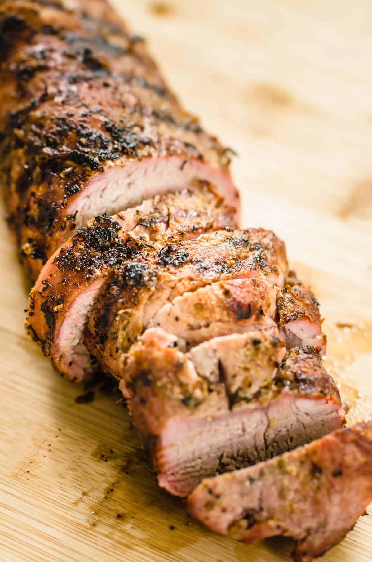 Grilled pork tenderloin, sliced on a cutting board.