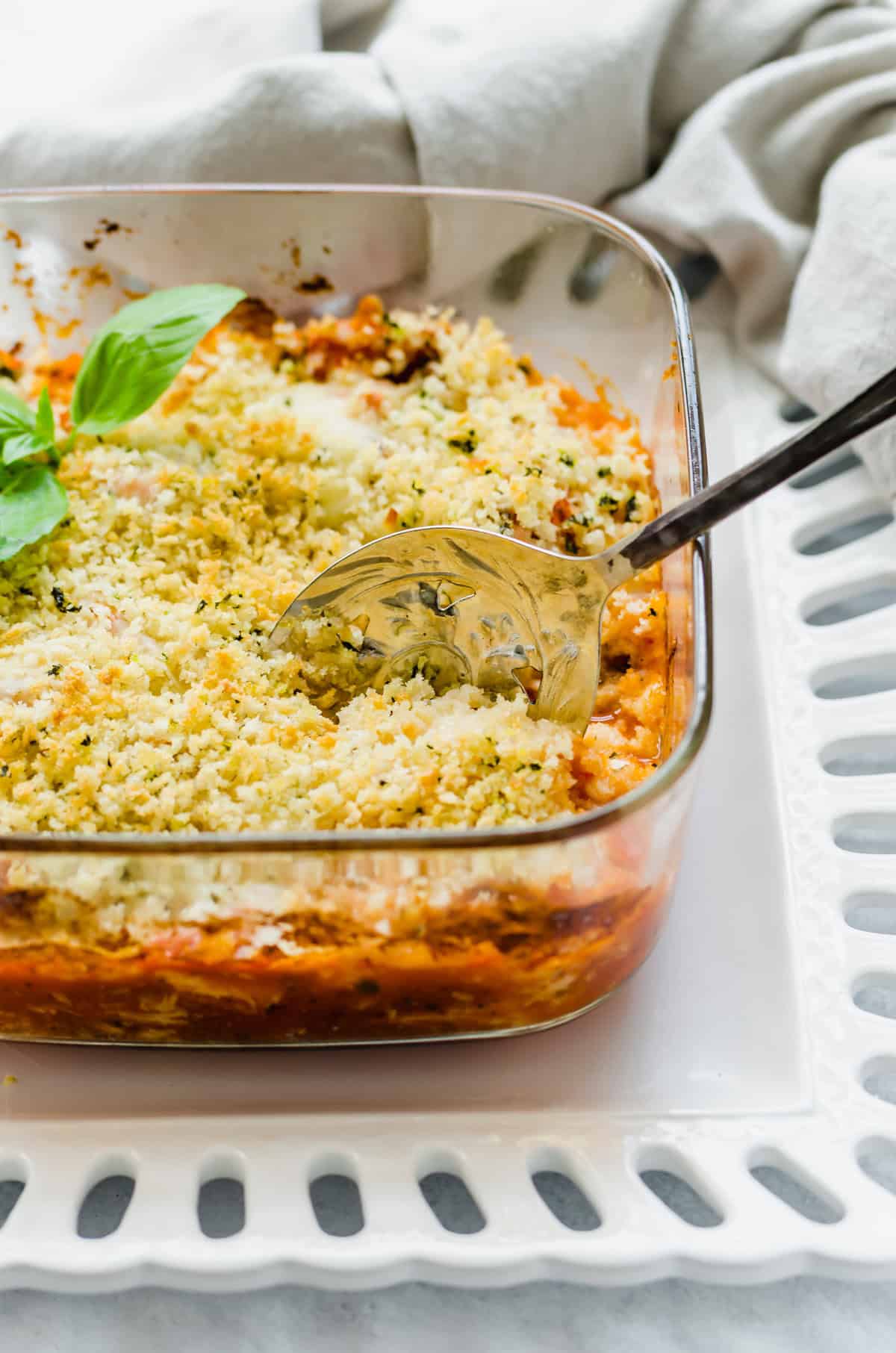 Chicken Parmesan casserole in a glass dish with a serving spoon scooping some out.