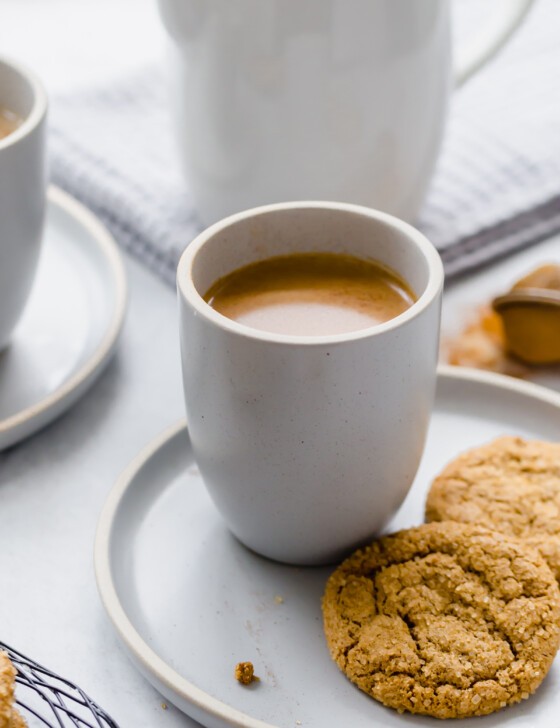 Pumpkin spice latte in a mug with two snickerdoodle cookies on a plate next to it.