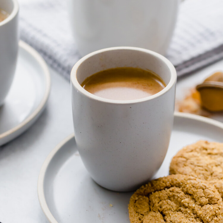 Pumpkin spice latte in a mug with two snickerdoodle cookies on a plate next to it.