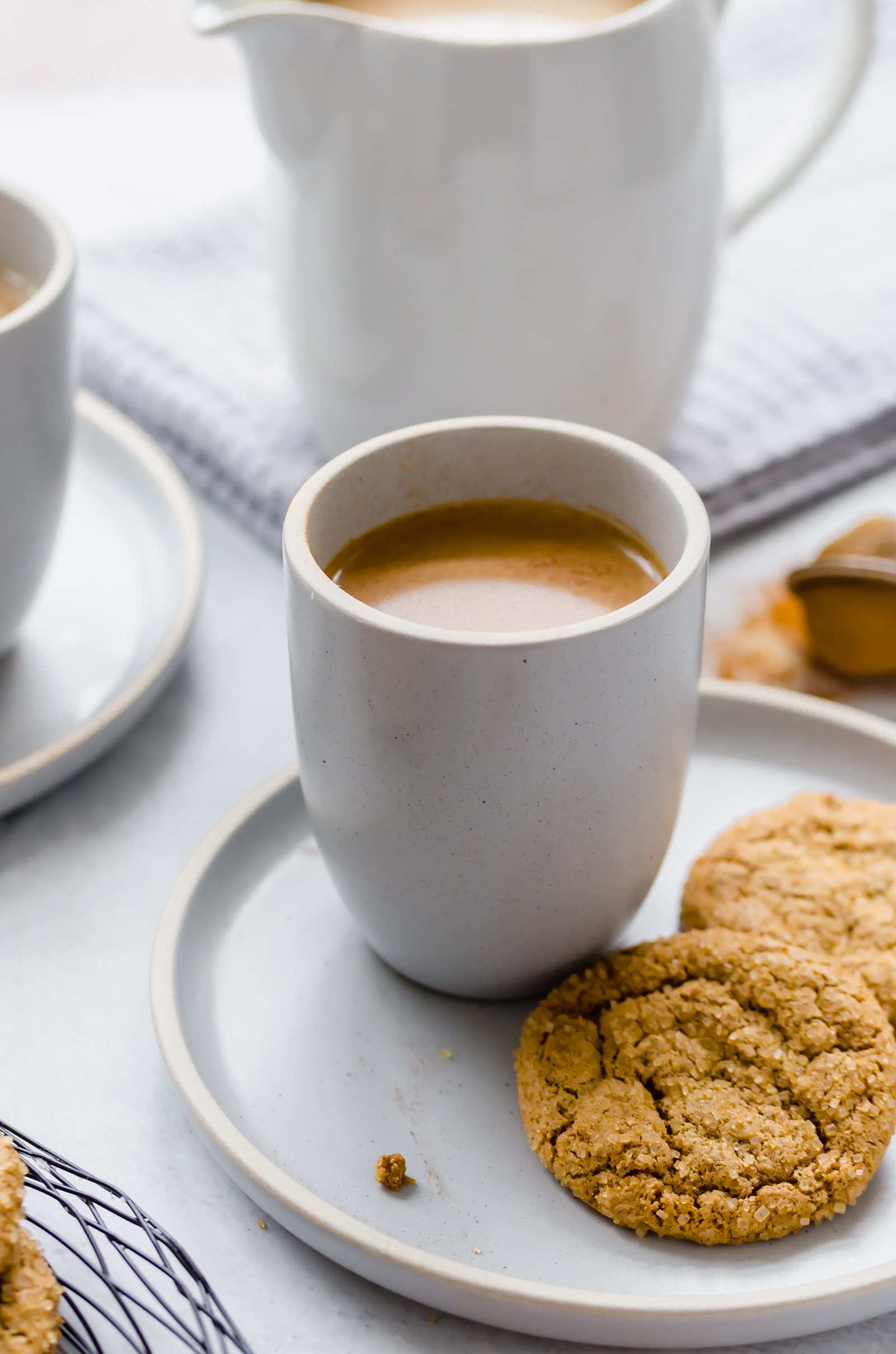 A mug of crock pot pumpkin spiced latte with two cookie on a plate next to it.