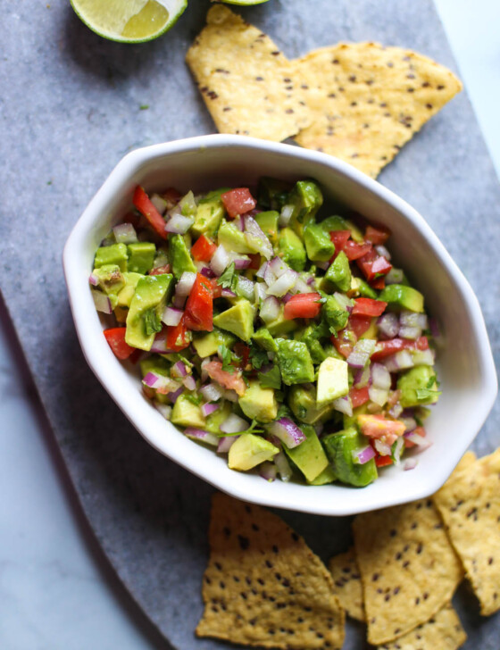Avocado salsa in a white bowl with chips surrounding it.