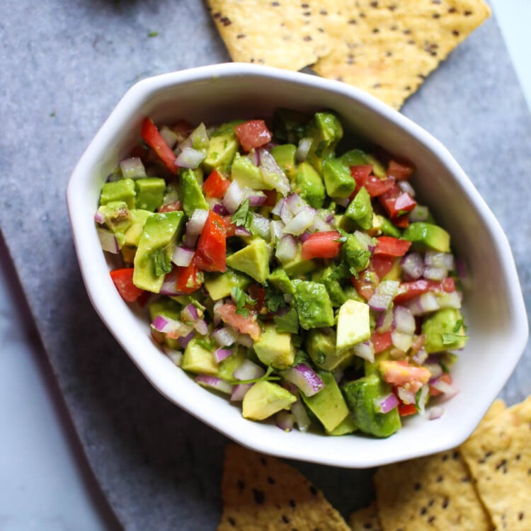 Avocado salsa in a white bowl with chips surrounding it.