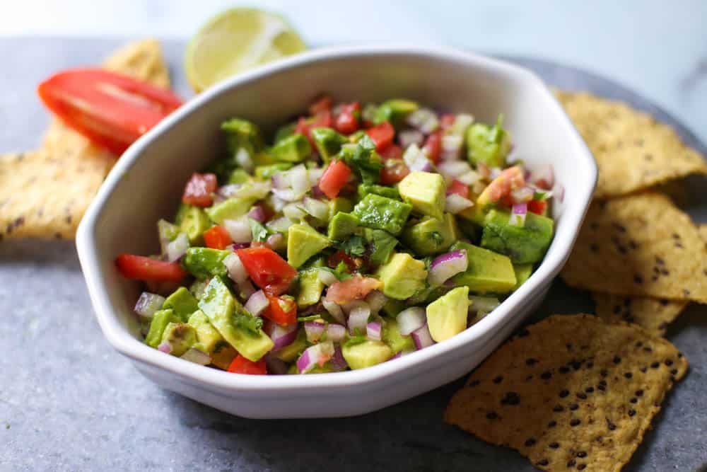 Avocado lime salsa in a white dish with chips surrounding it