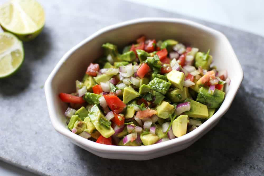 Avocado Lime Salsa in a white serving bowl with lime halves next to it.