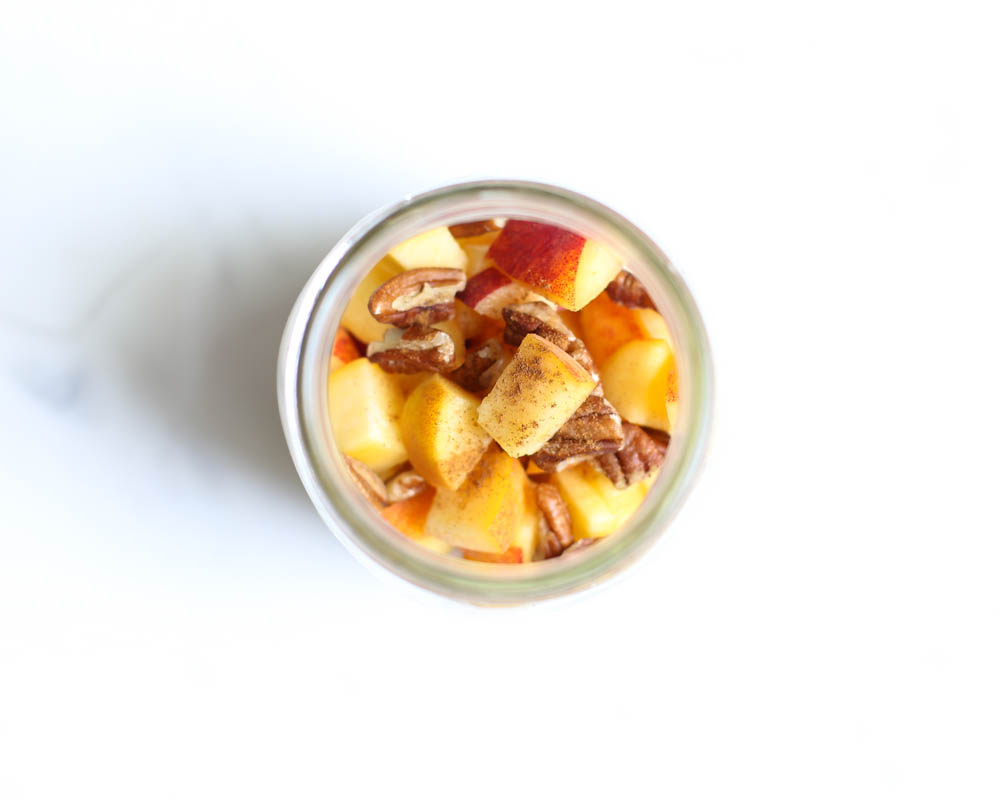 Looking into the top of a mason jar of peach overnight oats with cinnamon, chopped peaches, and pecans on top.