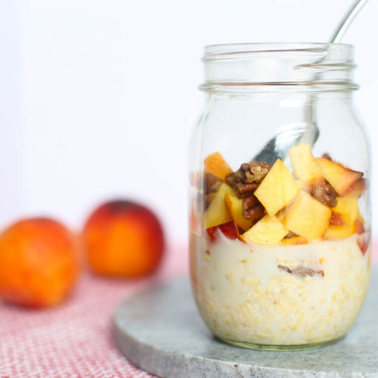 Peach overnight oats in a mason jar on a counter with a couple whole peaches nearby.