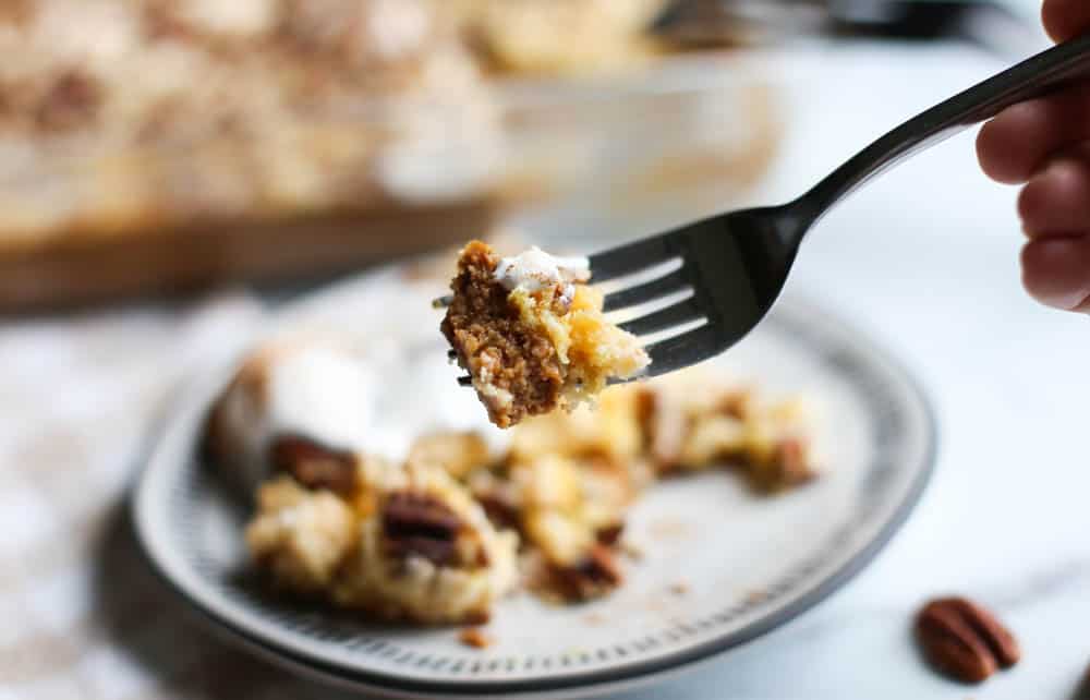 A bite of pumpkin dump cake on a fork above a plate with the pumpkin dump cake and whip cream.