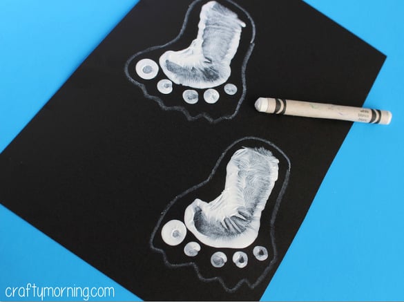 Footprint ghost craft for kids completed - black construction paper with white paint footprints on it.
