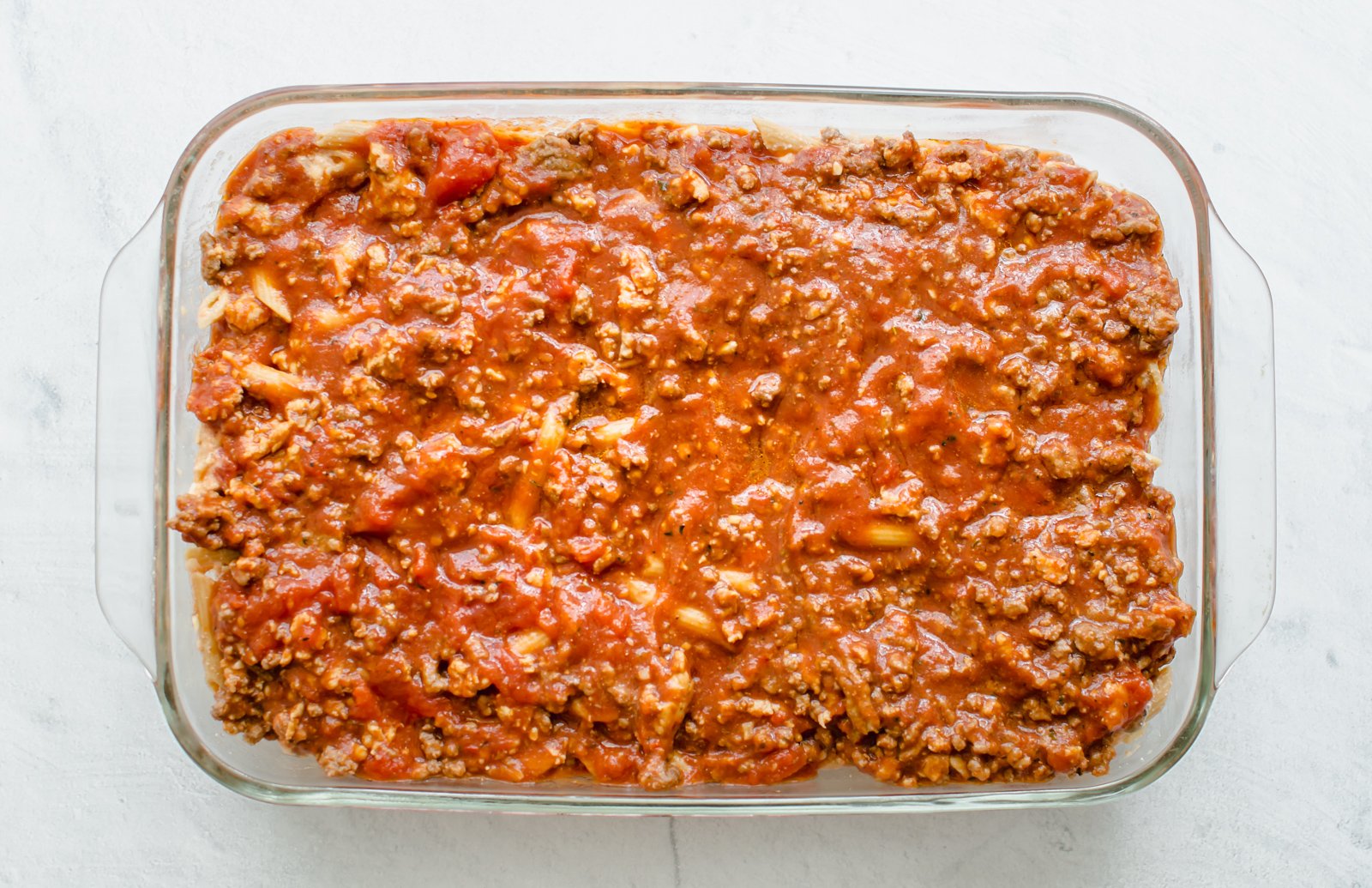 Meat sauce layered over cooked pasta in a 9x13 dish. 