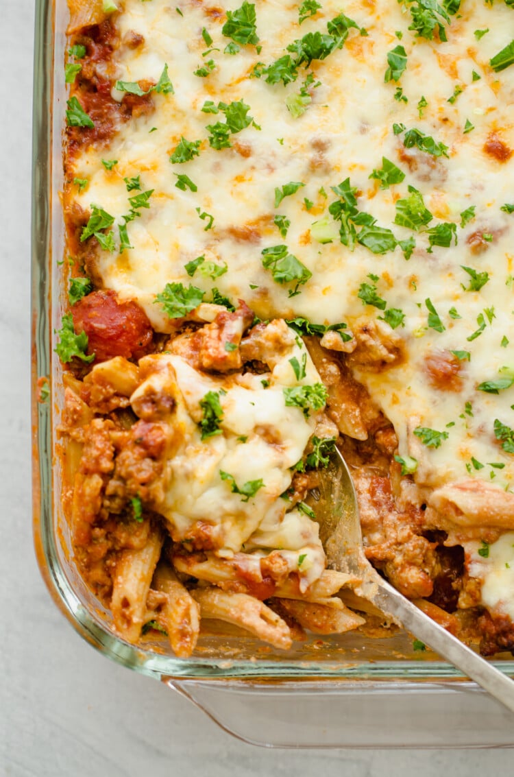 Baked penne pasta being scooped out of a glass baking dish.