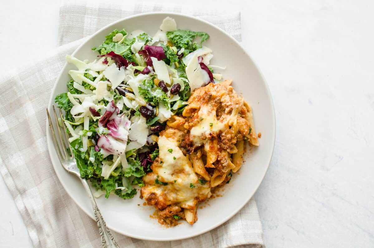 Baked Penne pasta on a white plate with salad.