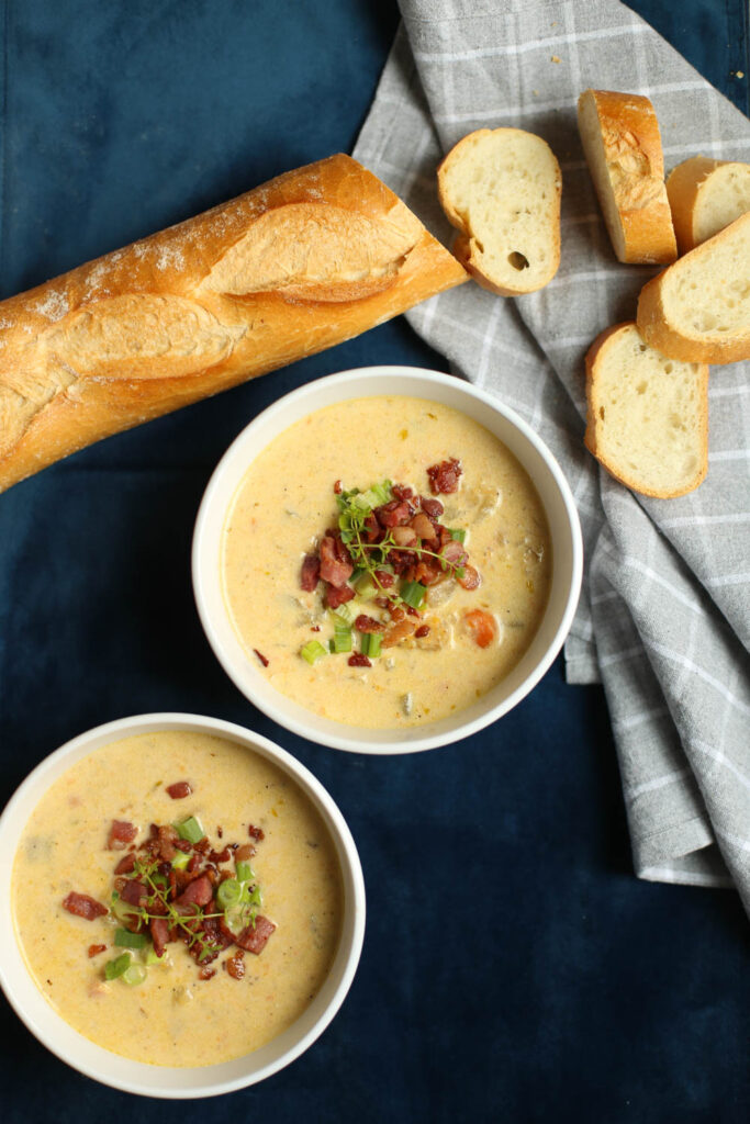 Slow Cooker Cheddar and Bacon Potato Soup in white bowls with bread.