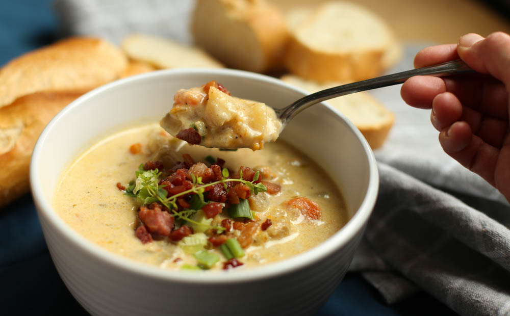 Slow Cooker Cheddar and Bacon Potato Soup in white bowl with bread.