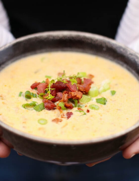 Cheddar and bacon potato soup in a bowl with chopped scallions and bacon on top.