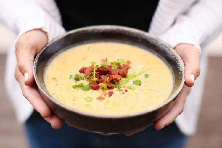 Cheddar and bacon potato soup in a bowl with chopped scallions and bacon on top.