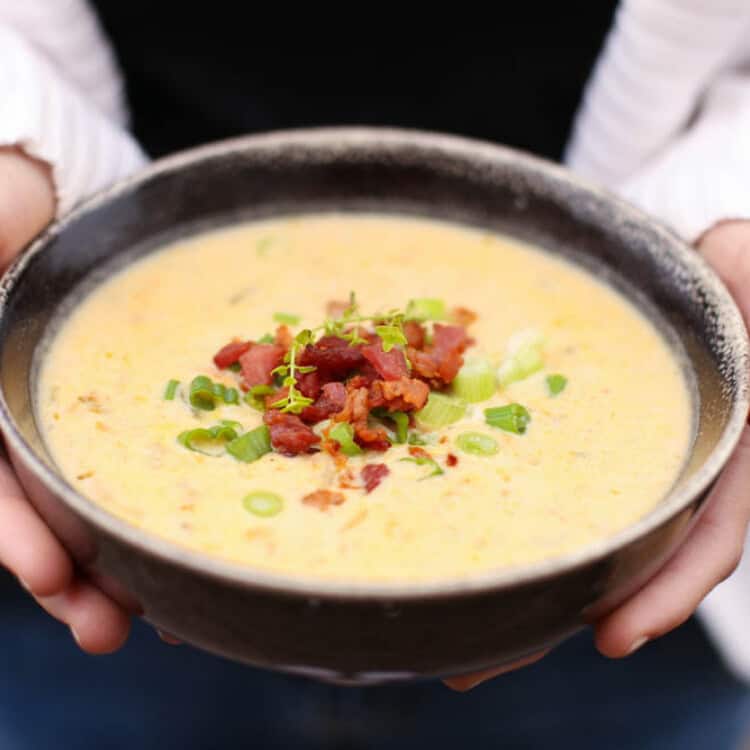 Cheddar and bacon potato soup in a bowl with chopped scallions and bacon on top.