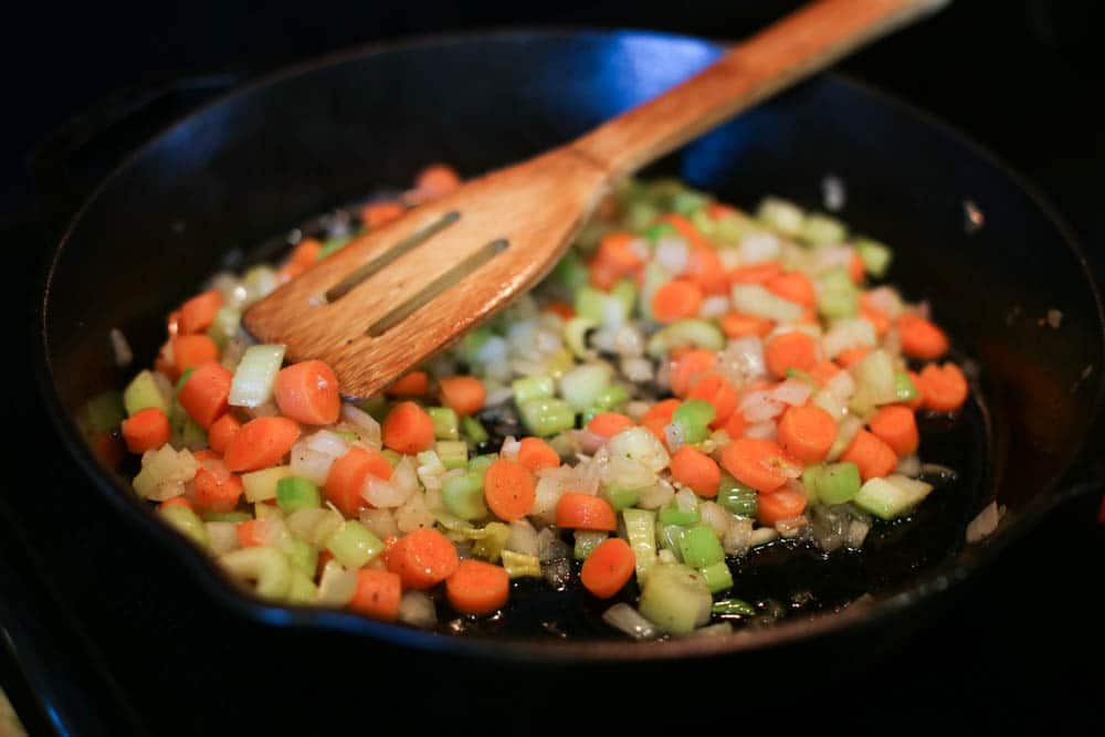 Carrots, celery, and onions sauteing in a cast iron skillet.