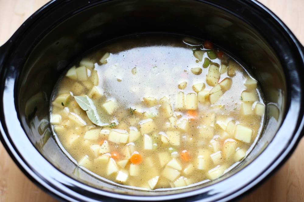 Potatoes, bay leaf, and carrots, onions, celery, chicken stock in a slow cooker.