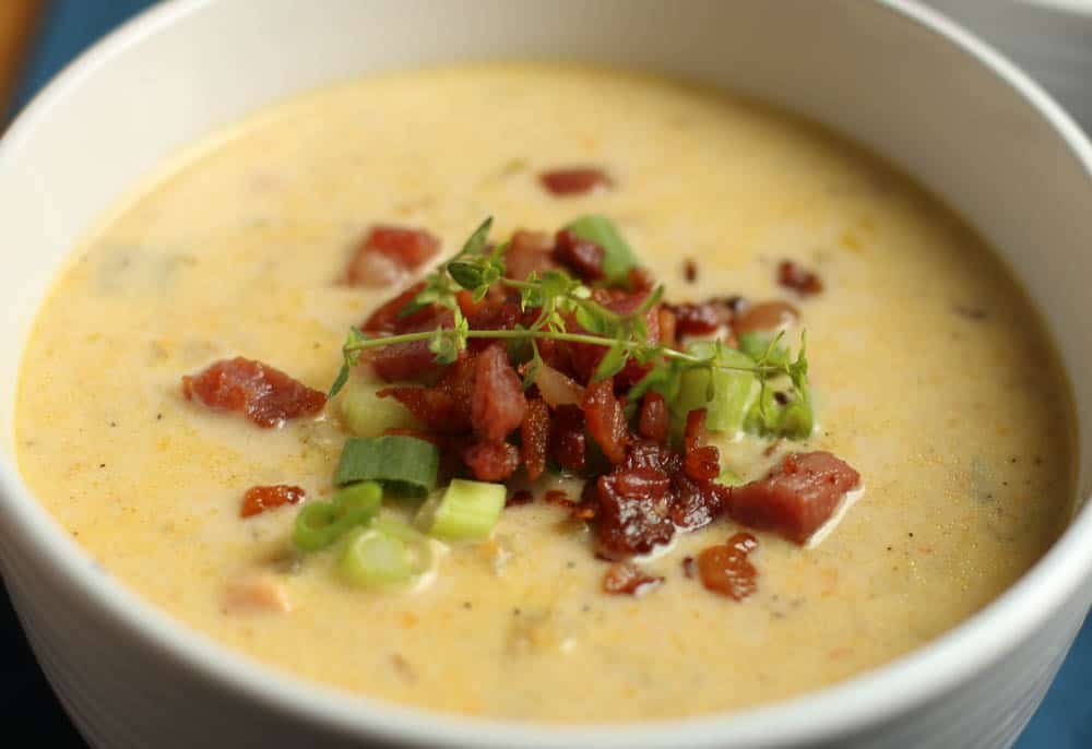 Slow Cooker Cheddar and Bacon Potato Soup in white bowl with chopped bacon and scallions on top.