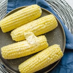 Four ears of corn on the cob on a plate with butter on top.