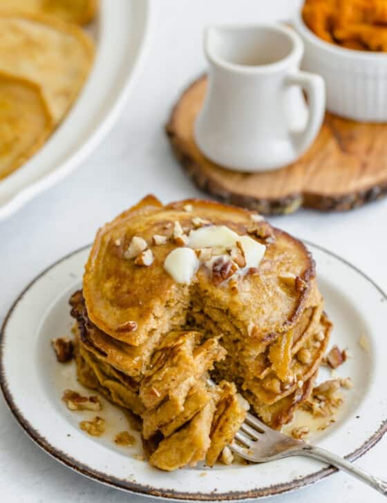 Whole wheat pumpkin pancakes stacked on a plate with pecans, butter, and syrup on top.