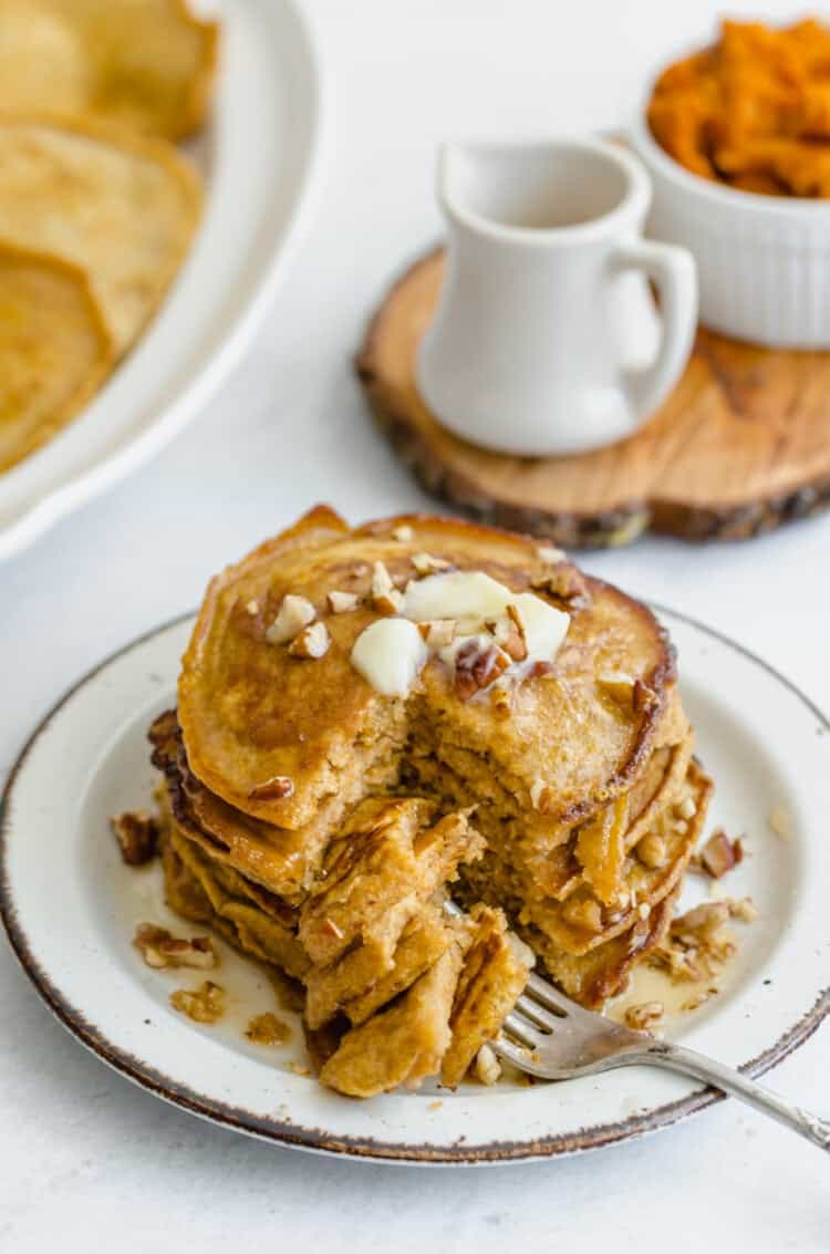 Whole wheat pumpkin pancakes stacked on a plate with pecans, butter, and syrup on top.