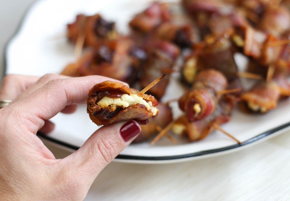 Woman holding a bacon-wrapped date with goat cheese.