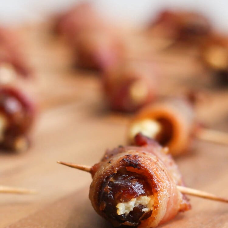 A Bacon-Wrapped Date with Goat Cheese sitting on a cutting board with more in the background.