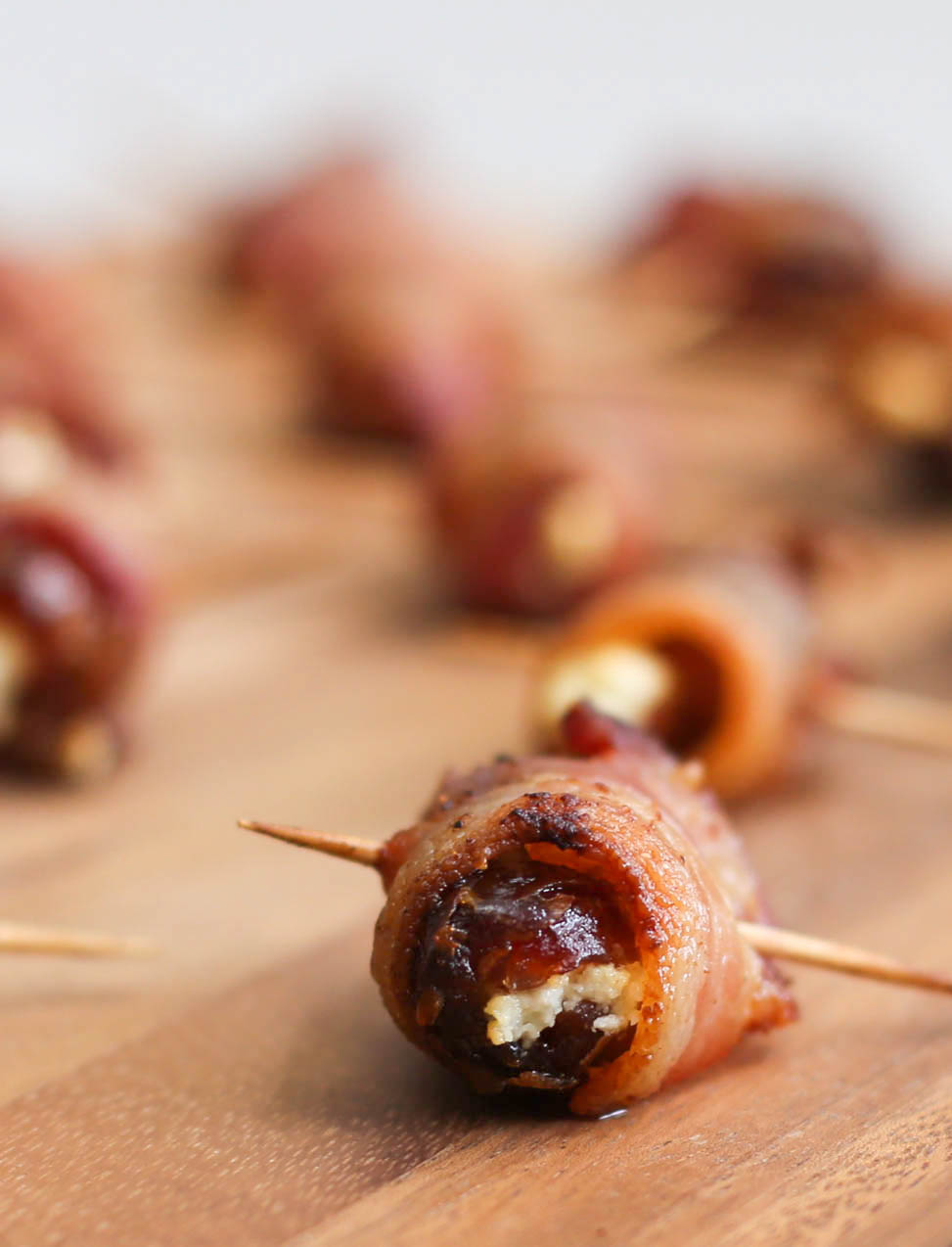 Bacon-Wrapped Dates with Goat Cheese on a cutting board.