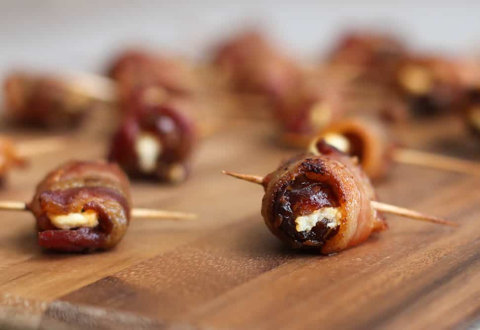 Bacon-Wrapped Dates with Goat Cheese lined up on a cutting board.