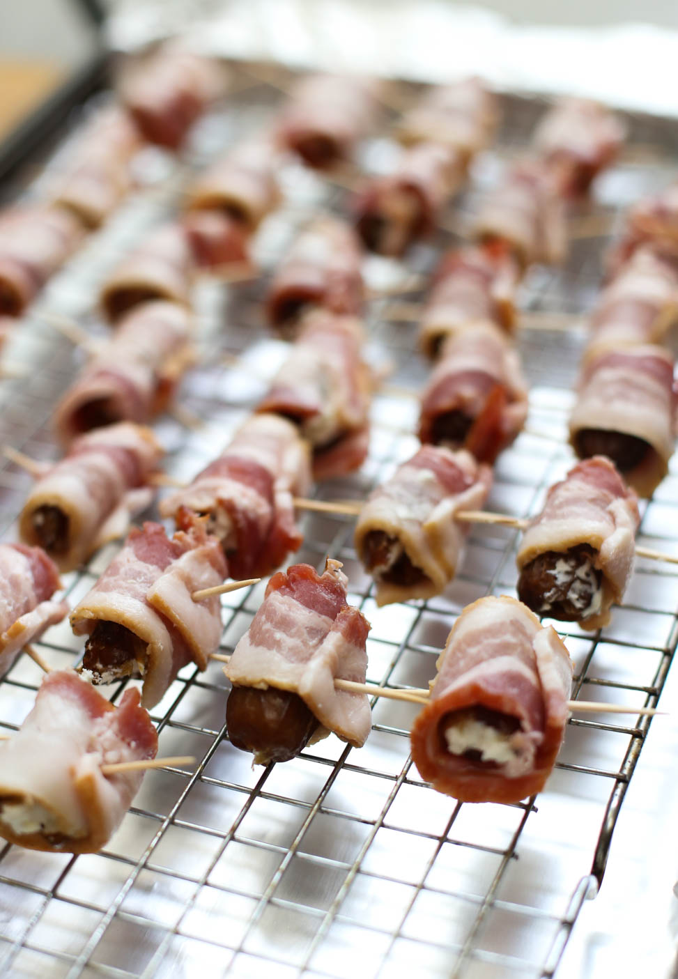 Bacon-Wrapped Dates with Goat Cheese on a baking rack ready for the oven.