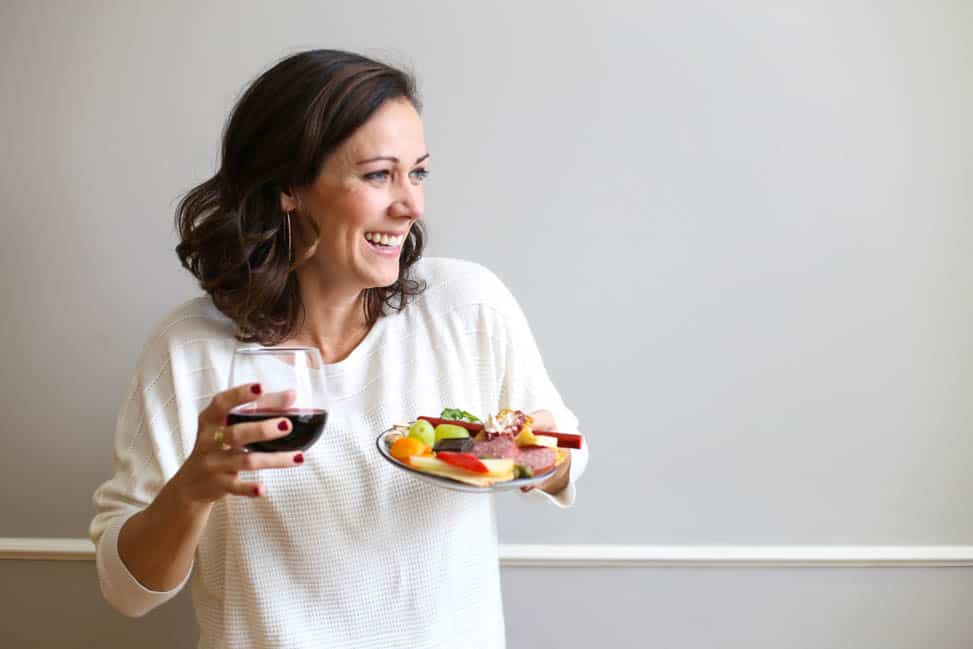 Woman holding wine in one hand and a plate with food in another hand.