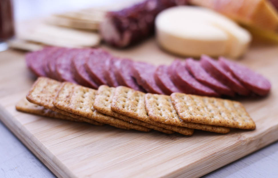 Crackers and summer sausage spread out on a cutting board.