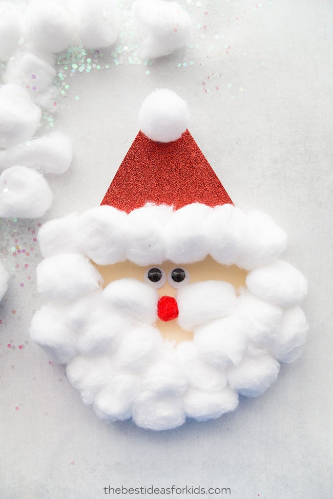 Santa face with lots of cotton balls around it for the beard and hair and one on top of a red hat.