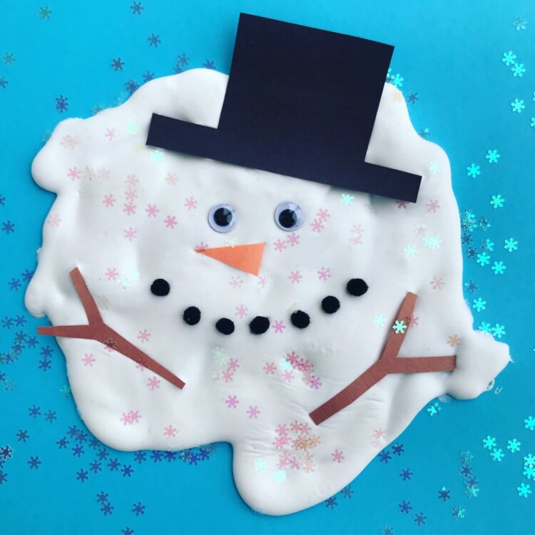 A melting snowman craft made of a large puddle of white glue wit google eyes, and orange triangle nose, a black tophat, brown paper arms like twigs, and black pom poms for the mouth.