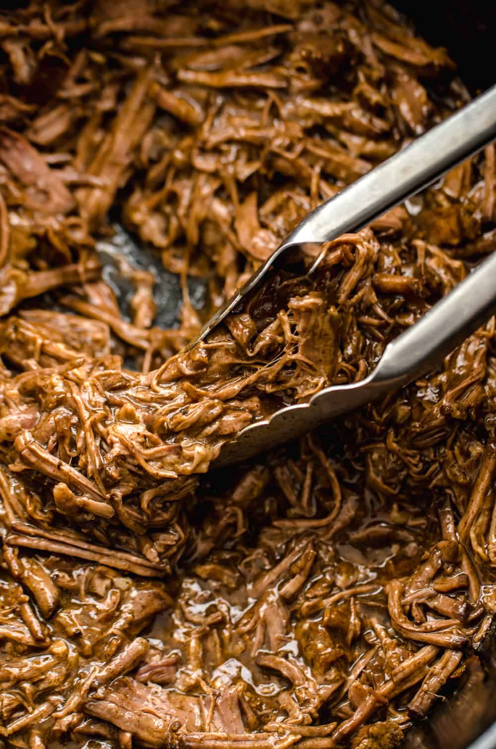 Shredded beef being picked up with metal tongs.