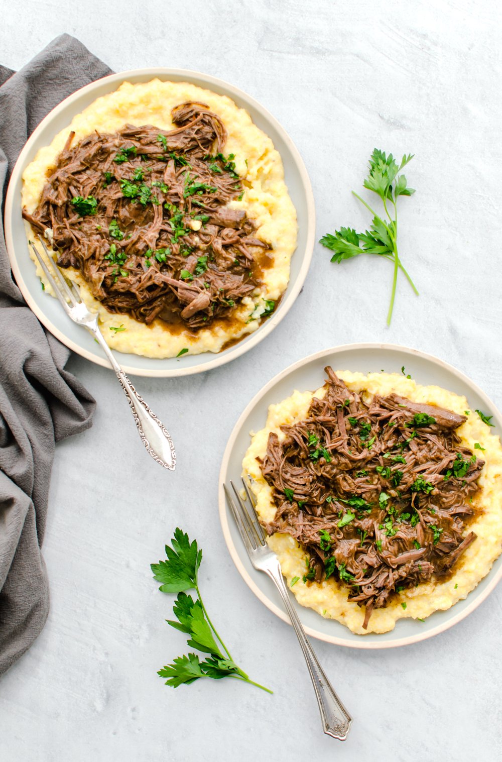 Balsamic shredded beef and sauce over polenta on two plates.