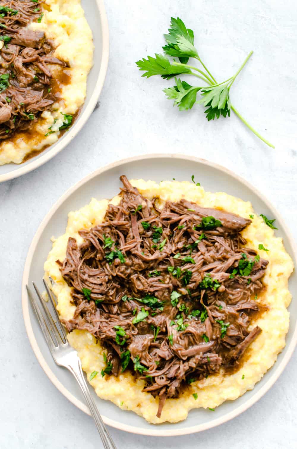 Balsamic shredded beef on top of polenta with chopped parsley on top.