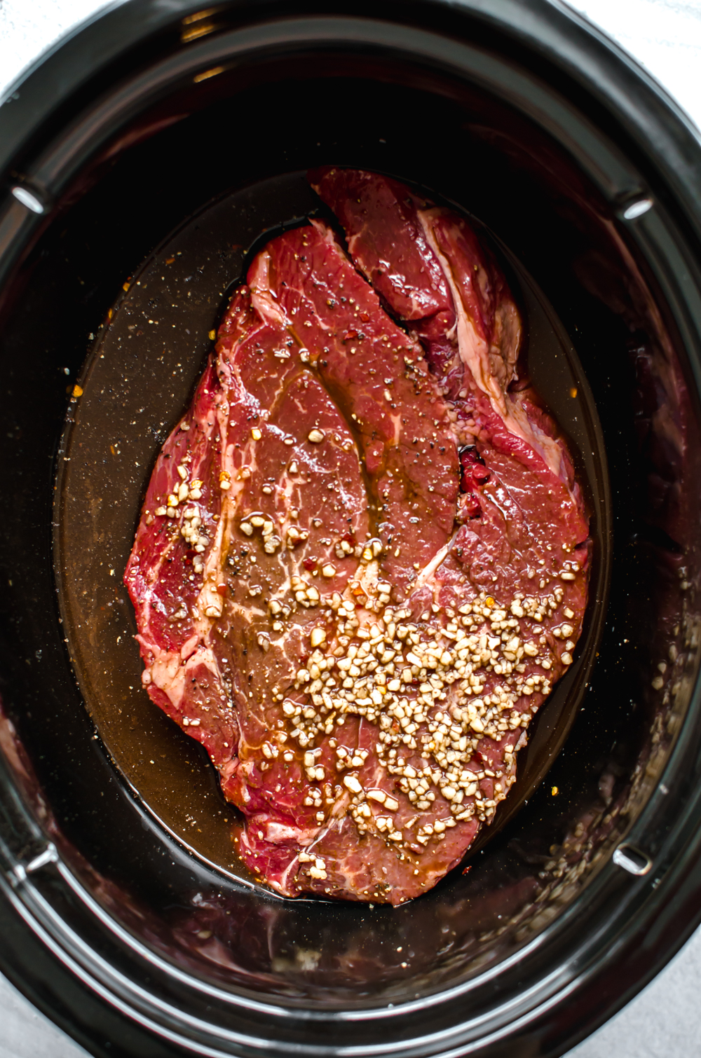 Seasoned chuck roast in a slow cooker getting ready to be cooked.