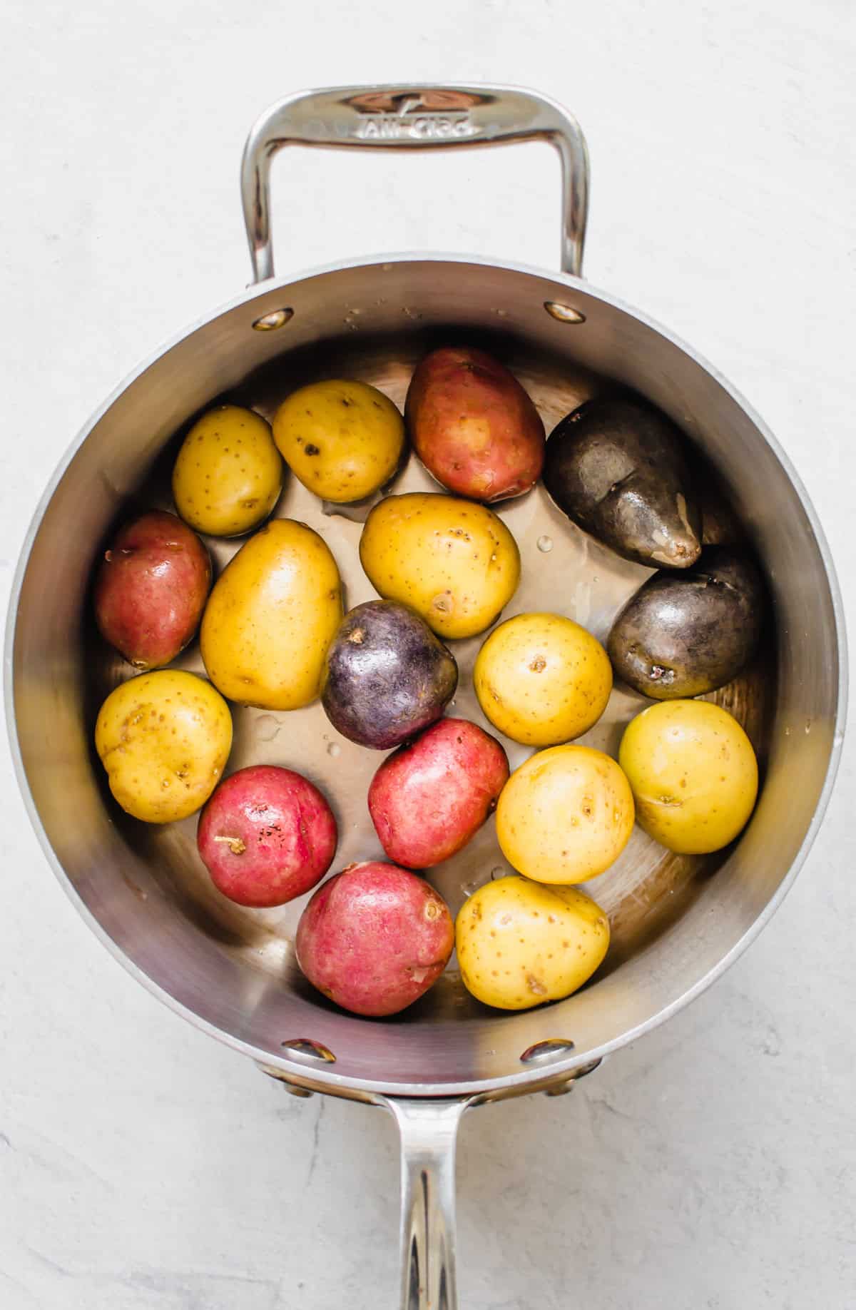 Washed purple, red, and yellow baby potatoes in a metal pot.