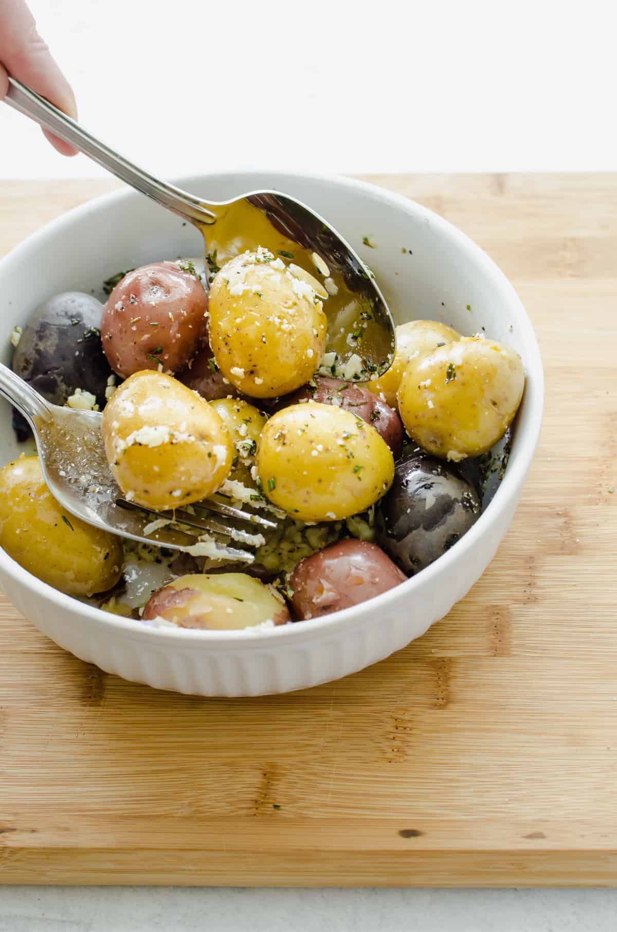 Boiled baby potatoes served in a white bowl with Parmesan and chopped parsley on top.