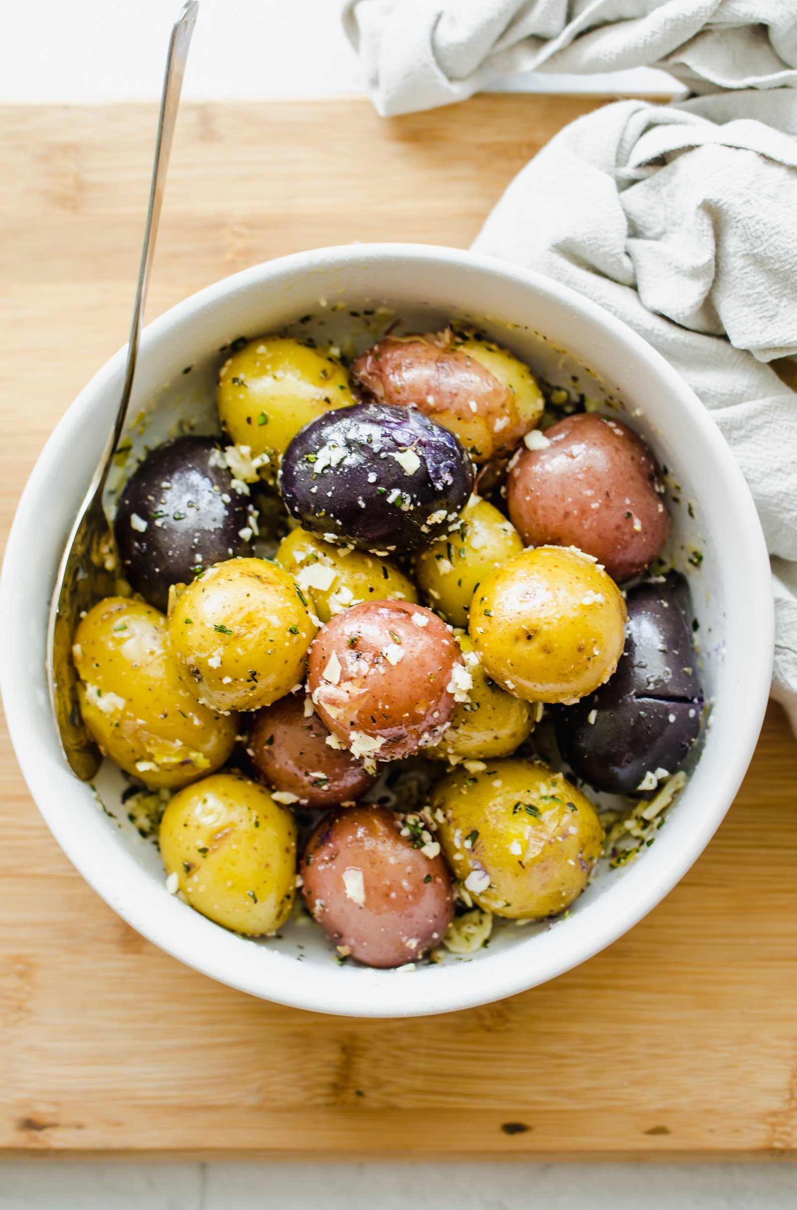 Boiled red, blue, and yellow baby potatoes in a white bowl with Parmesan and chopped fresh parsley.