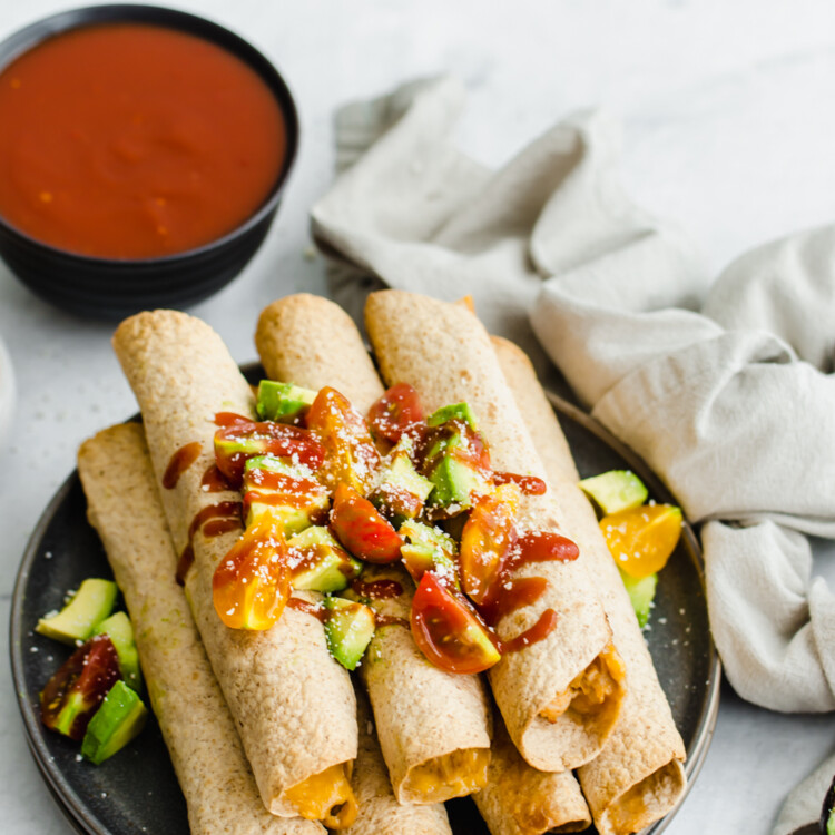 Creamy Chicken Taquitos stacked up on a plate with a bowl of salsa next to it.