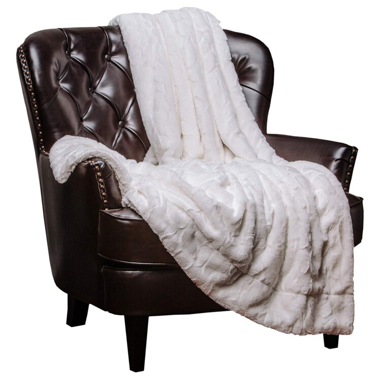 A brown leather upright chair with a white faux fur blanket thrown across it.